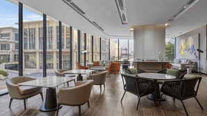 A modern lounge area with large windows, comfortable seating, and a view of the cityscape.