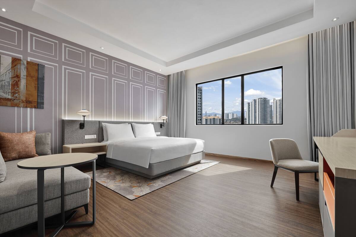 Una habitación de hotel moderna con una cama grande, un sofá, un escritorio y vistas a la ciudad.