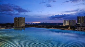 A large, rectangular swimming pool with a grid pattern, surrounded by high-rise buildings and a cityscape at dusk.