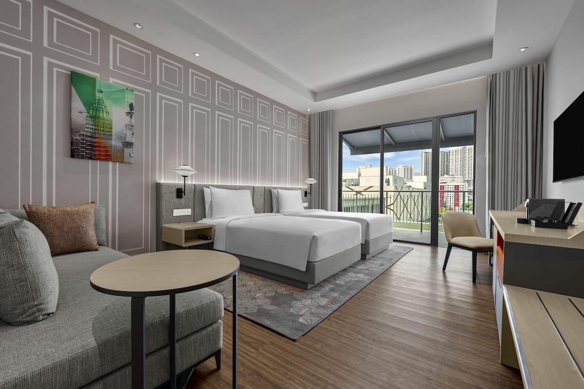 Una habitación de hotel moderna con una cama grande, un sofá, un escritorio y un balcón con vistas a la ciudad.