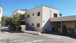 Un edificio de fachada plana, antenas parabólicas y zona exterior con mesas y sillas.