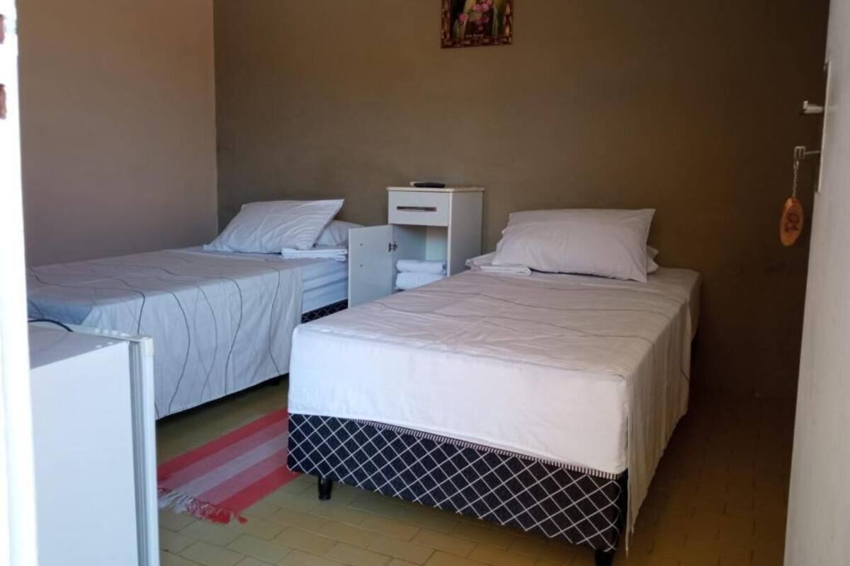 A room with two beds, a small white cabinet, a red and white striped rug, and a religious painting on the wall.