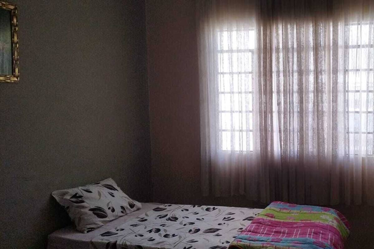 A bedroom with a bed, a fan, and a window with curtains.