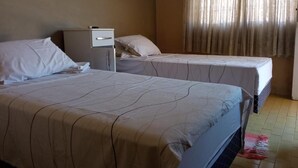 Una habitación de hotel con dos camas, una mesita de noche y una ventana con cortinas.