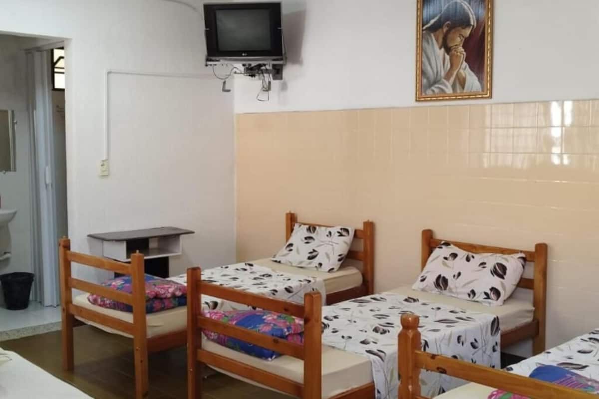 A room with three wooden beds, a television mounted on the wall, and a painting above the beds.