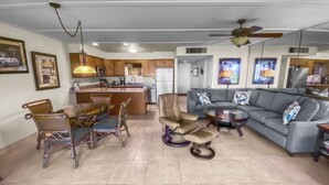 A modern living room with a grey sofa, a dining table with chairs, and a kitchen area in the background. - Maalaea Surf #g-2 1 Bedroom Condo by RedAwning (Kihei)