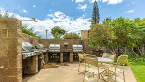An outdoor barbecue area with stone walls, multiple grills, and a table with chairs. - Maalaea Surf #g-2 1 Bedroom Condo by RedAwning (Kihei)