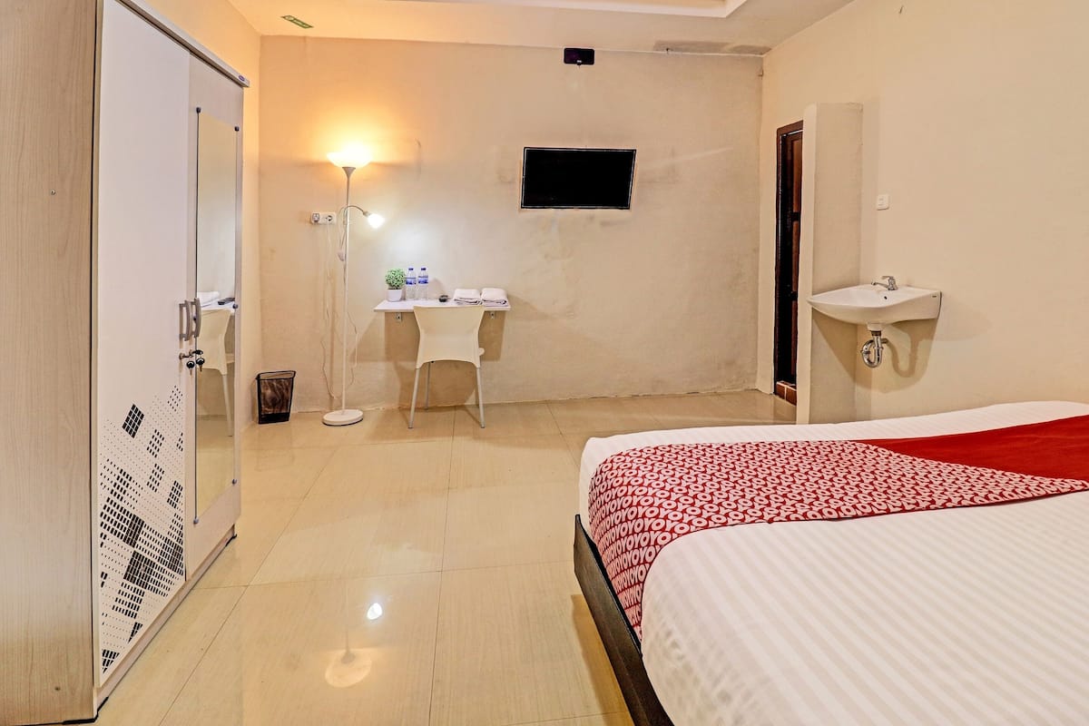 A hotel room with a bed, a desk, a chair, a TV, and a bathroom with a sink.