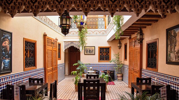 A courtyard with a tiled floor, wooden doors, and a central table with chairs. - riad zanouba (Marrakech)