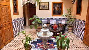 A courtyard with a fountain, potted plants, a sofa, and a wall with a geometric tile pattern. - riad zanouba (Marrakech)