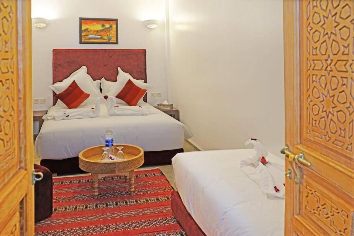 Habitación de hotel con dos camas, un tapete estampado, una mesita con una botella de agua y un cuadro en la pared.