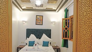 A hotel room with a large bed, two bedside tables, a decorative ceiling, and a wall-mounted artwork. - riad zanouba (Marrakech)