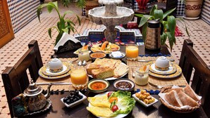 A traditional Moroccan dining table with a fountain centerpiece, surrounded by various dishes and drinks. - riad zanouba (Marrakech)