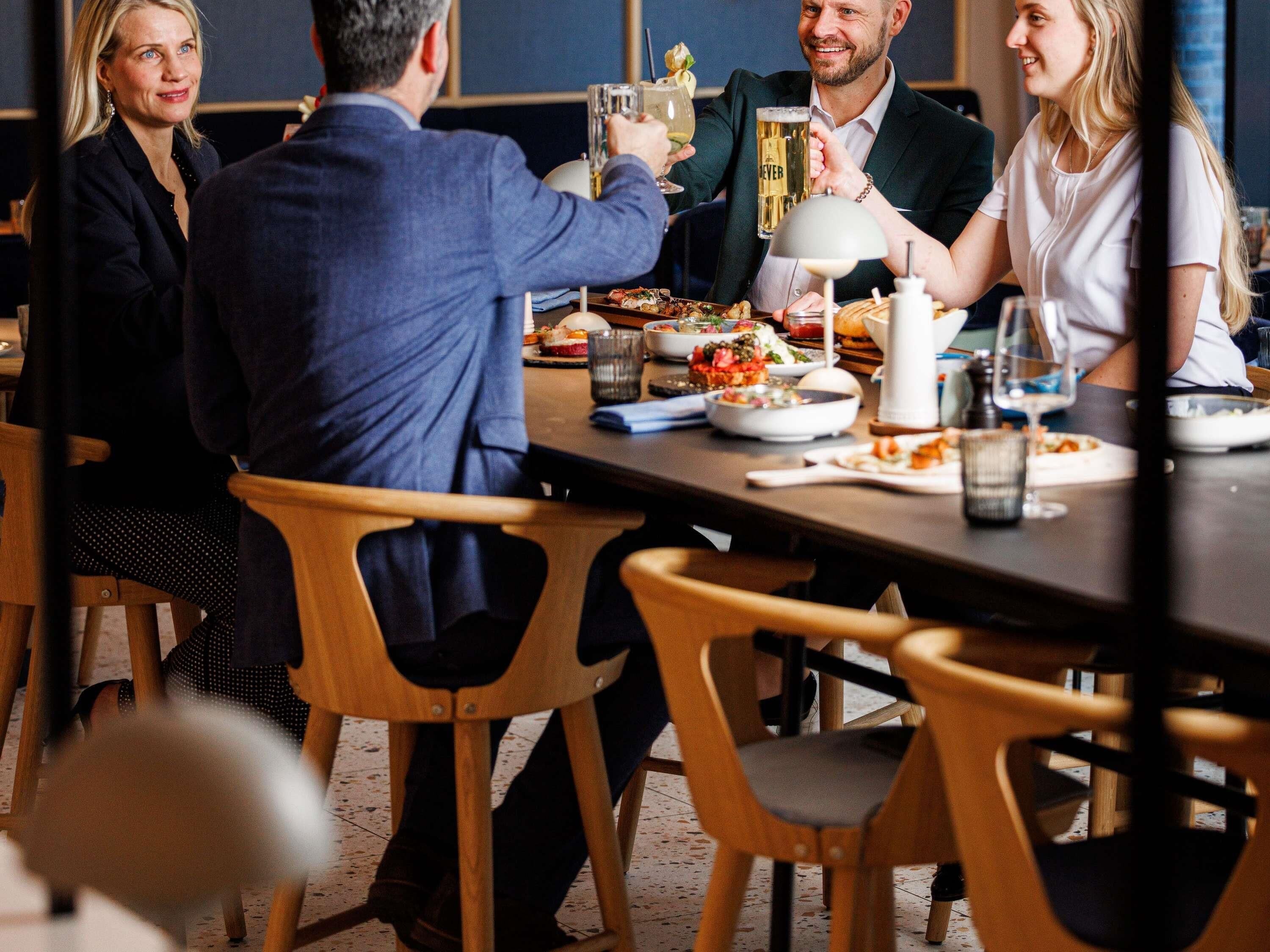 Un groupe de personnes est assis à une table, devant divers plats et boissons, ce qui laisse supposer qu’il s’agit d’un repas.