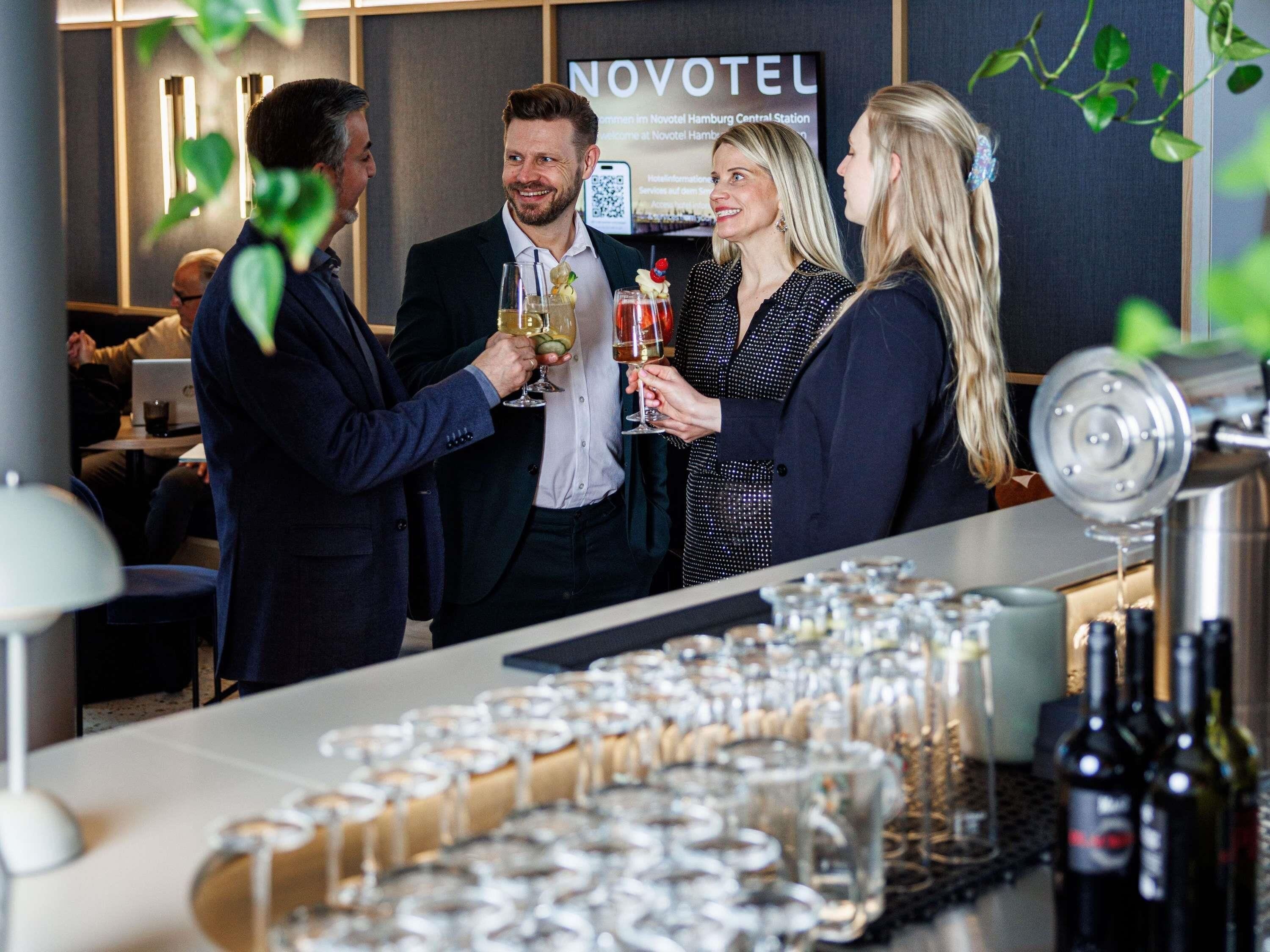 Zona de bar con vasos y botellas, un letrero de Novotel y un ordenador portátil sobre una mesa.