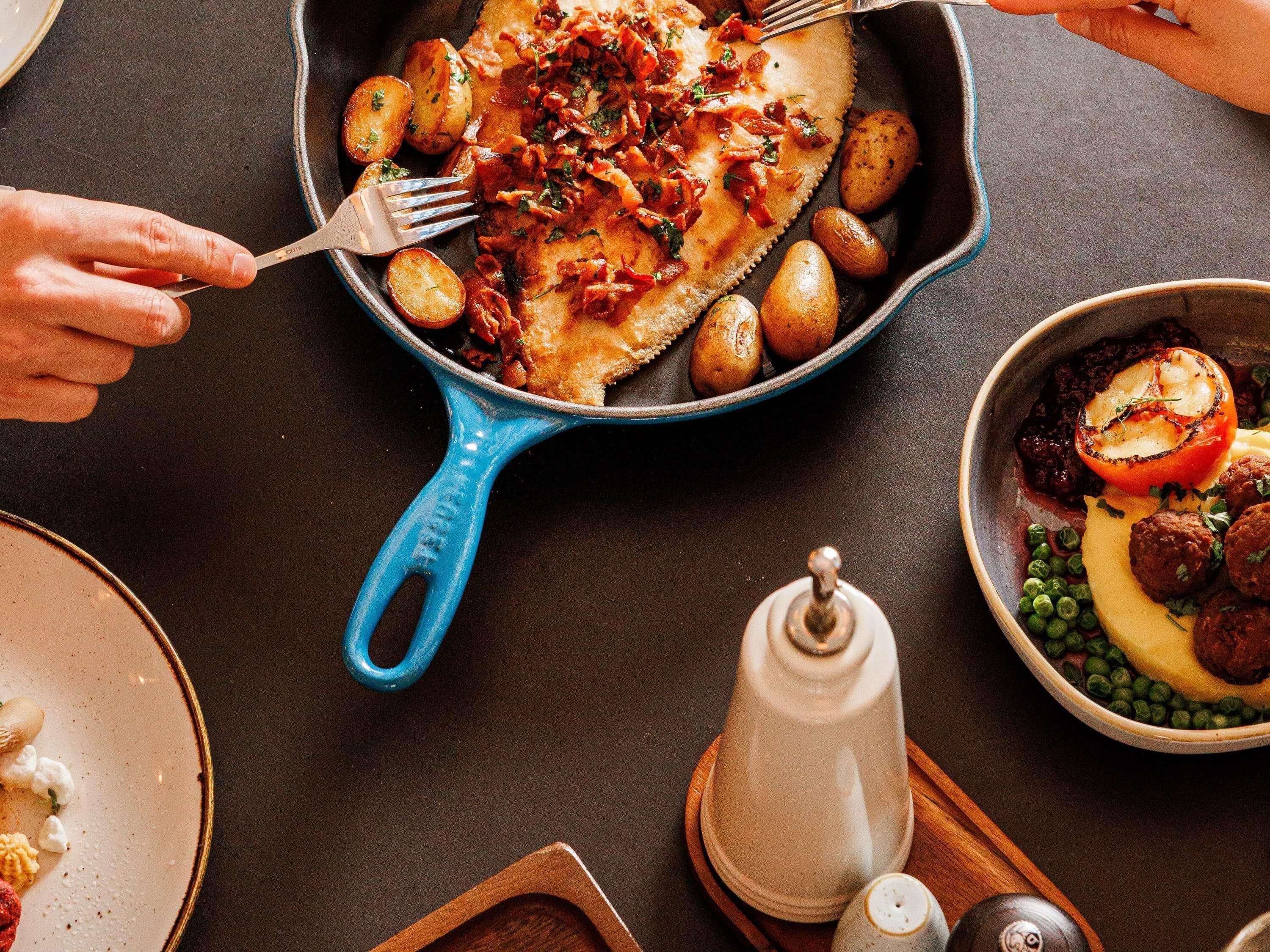 Une poêle bleue contenant des aliments, un moulin à poivre et un salier, le tout posé sur une table.