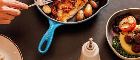 Une poêle bleue contenant des aliments, un moulin à poivre et un salier, le tout posé sur une table.