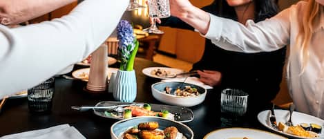 A group of people toasting with drinks at a table with various dishes, including sushi and a bowl of food.