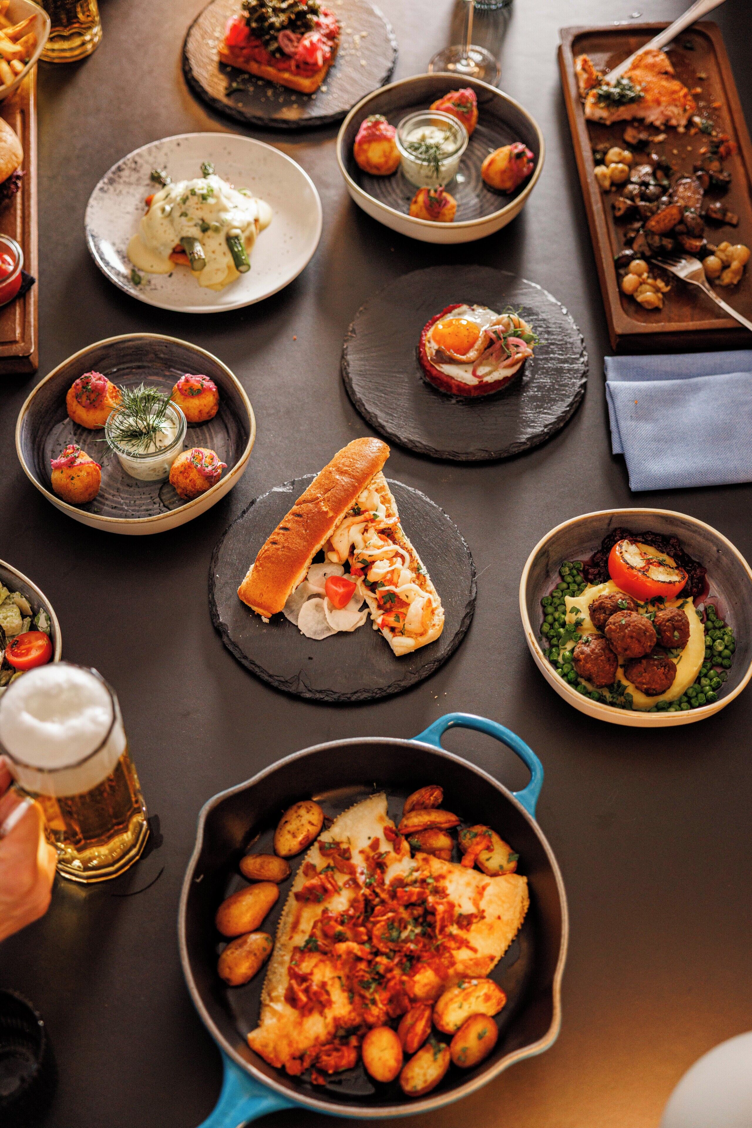 Une variété de plats sont disposés sur la table, notamment un filet de poisson accompagné de pommes de terre, un petit pain et plusieurs petites assiettes contenant différents amuse-gueules.