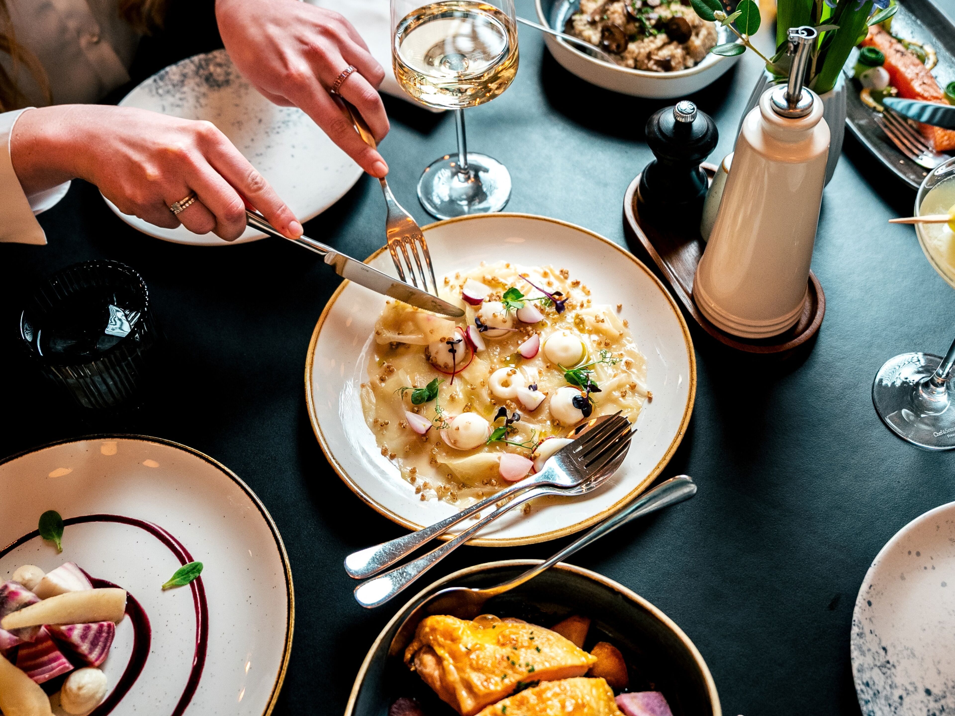 A dining table with plates of food, a wine glass, and a salt and pepper shaker.