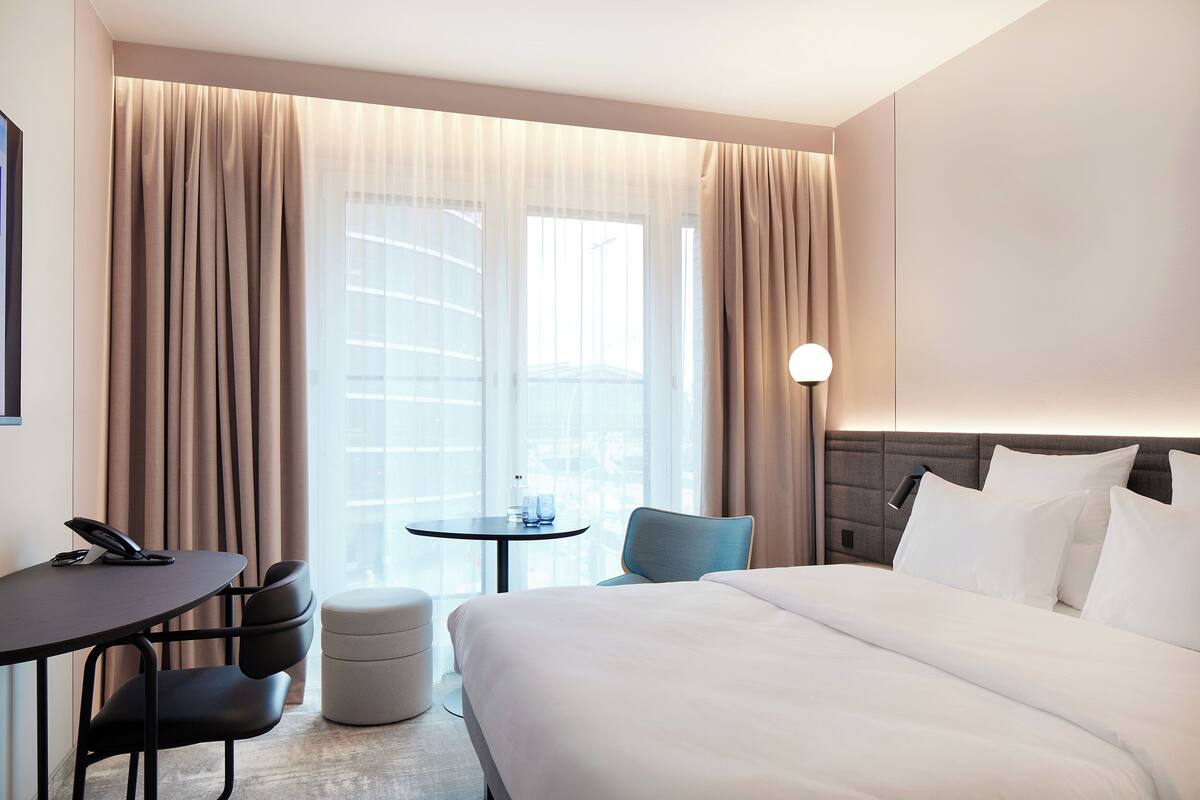 Une chambre d’hôtel avec un lit, un bureau, une chaise, une petite table et une lampe.