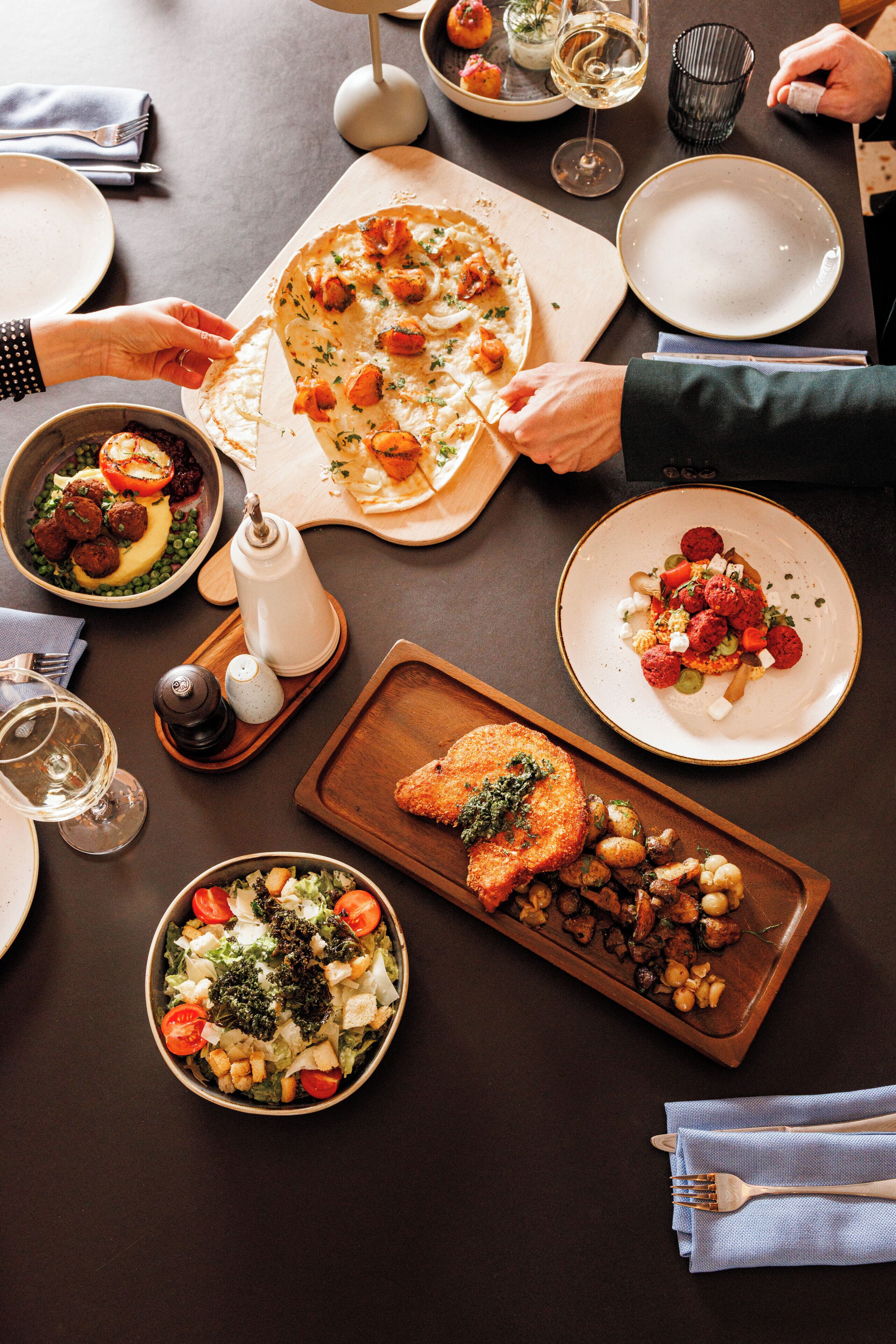 Een eettafel met verschillende gerechten, waaronder pizza, salade en geroosterde groenten.