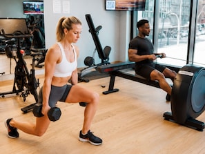 Een sportschool met trainingsapparatuur, een televisiescherm en een raam met uitzicht op buiten.