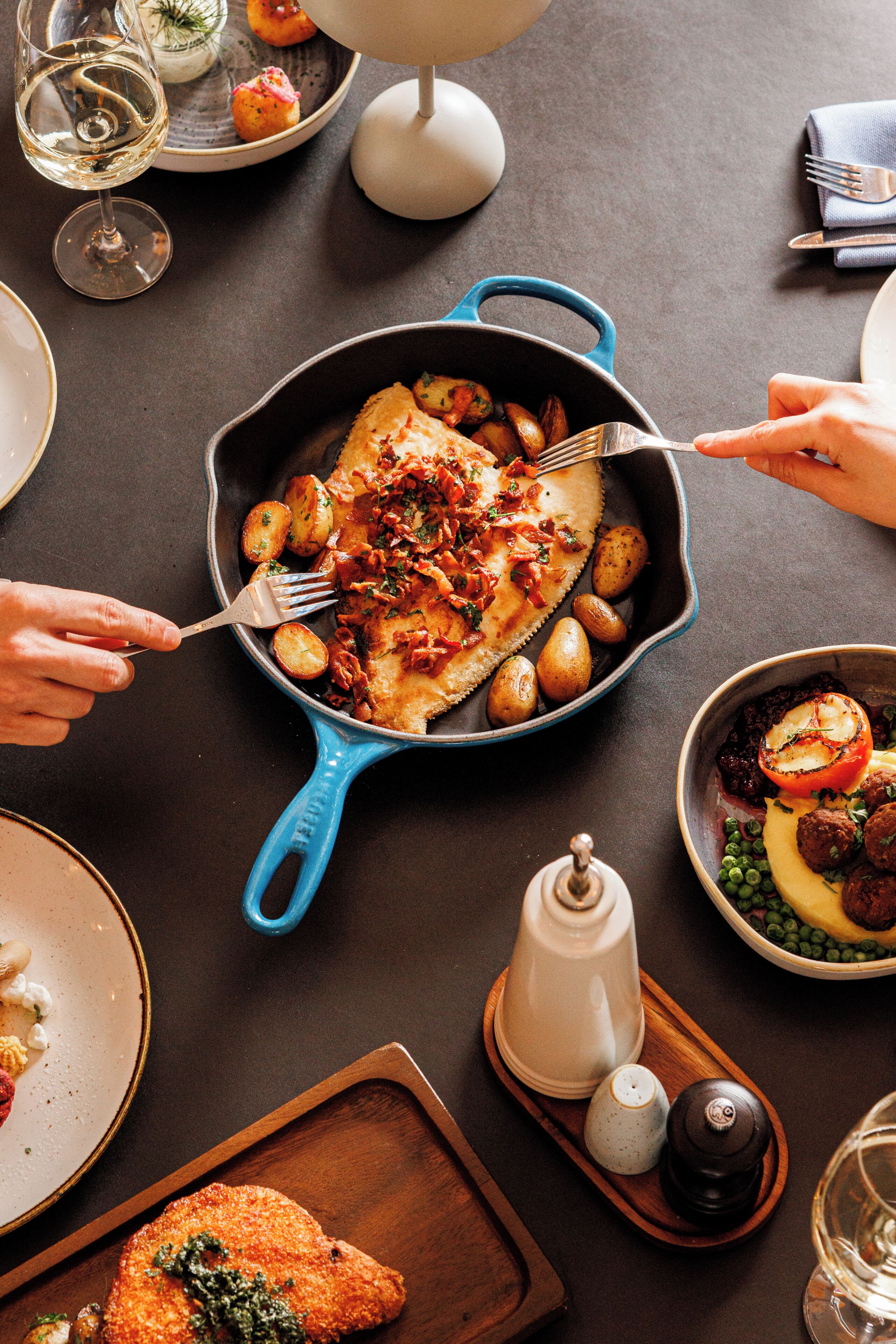 A dining table with a blue skillet containing food, a white salt shaker, and a pepper grinder.