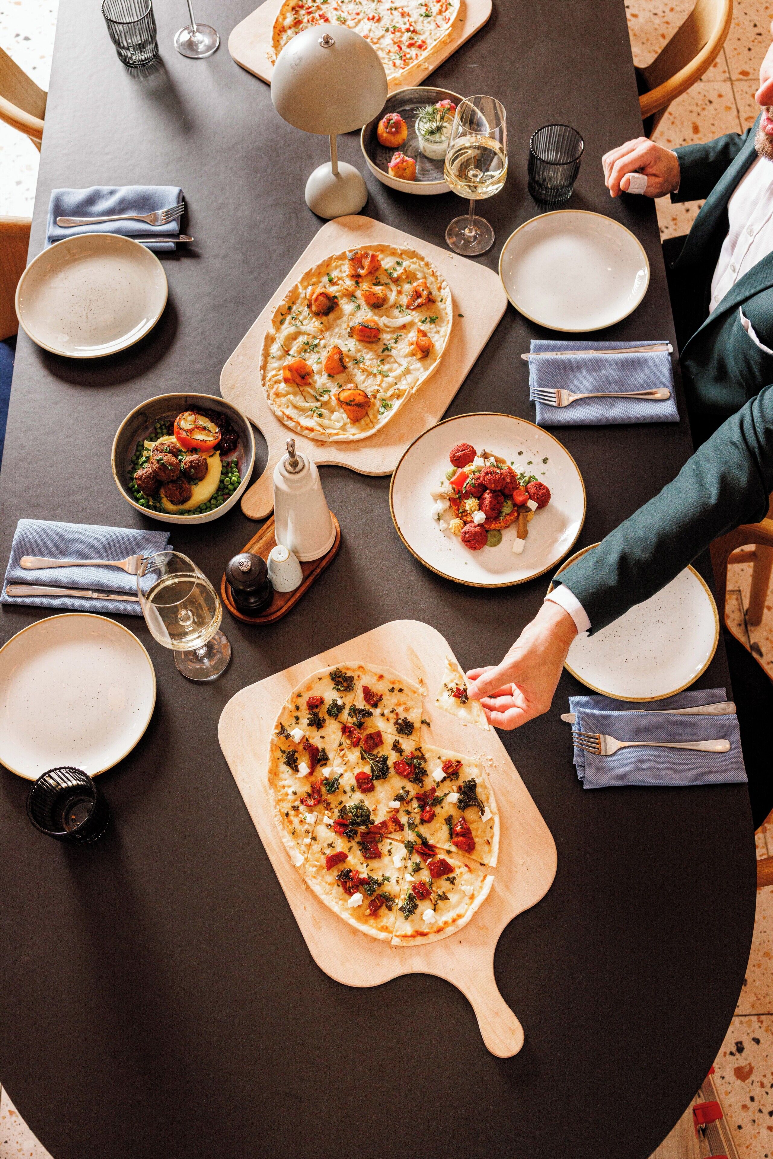 A dining table with various dishes, including pizzas and a bowl of salad, set for a meal.