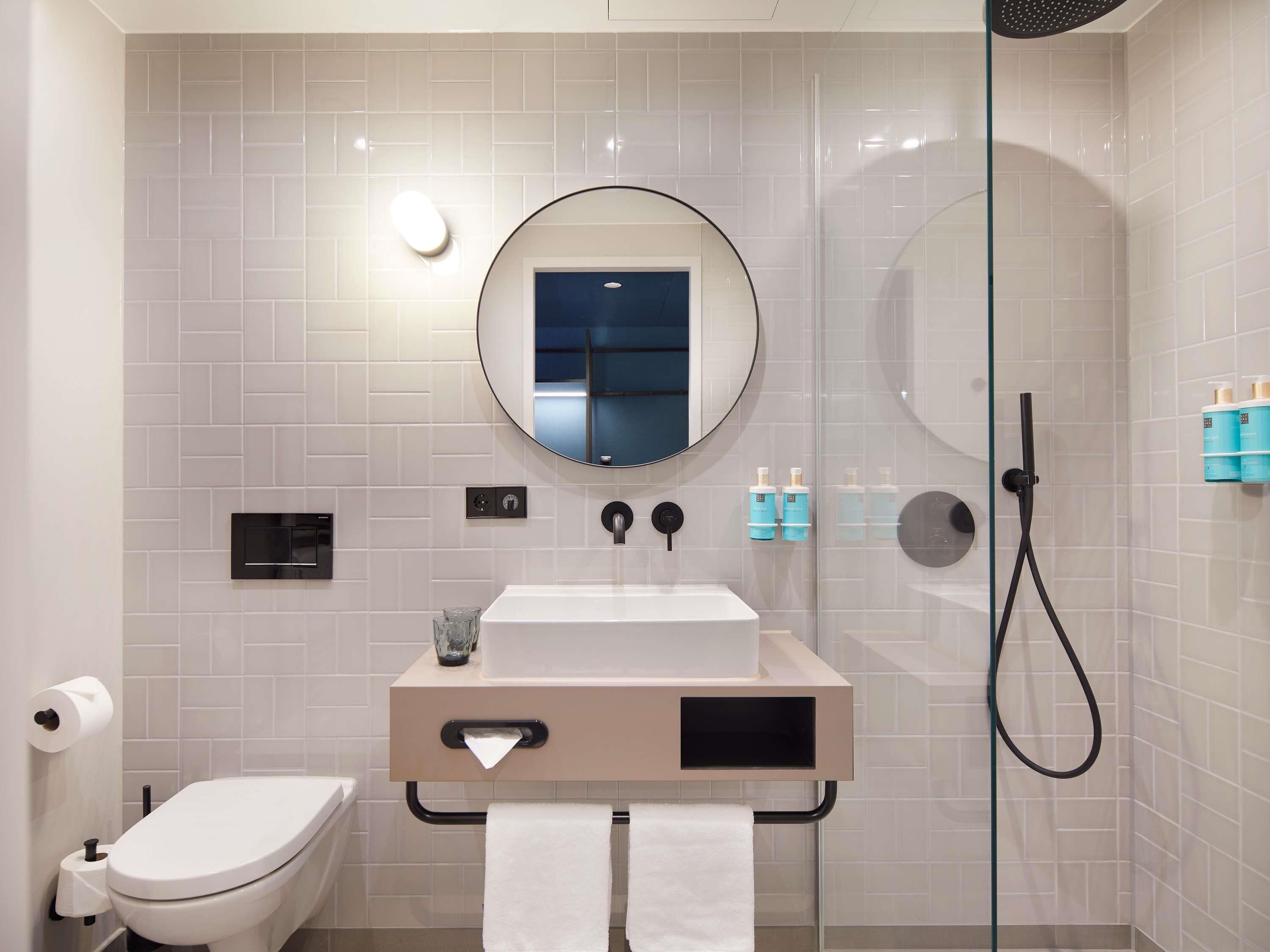 Ein modernes Badezimmer mit Toilette, Waschbecken, Spiegel und Duschkabine aus Glas.