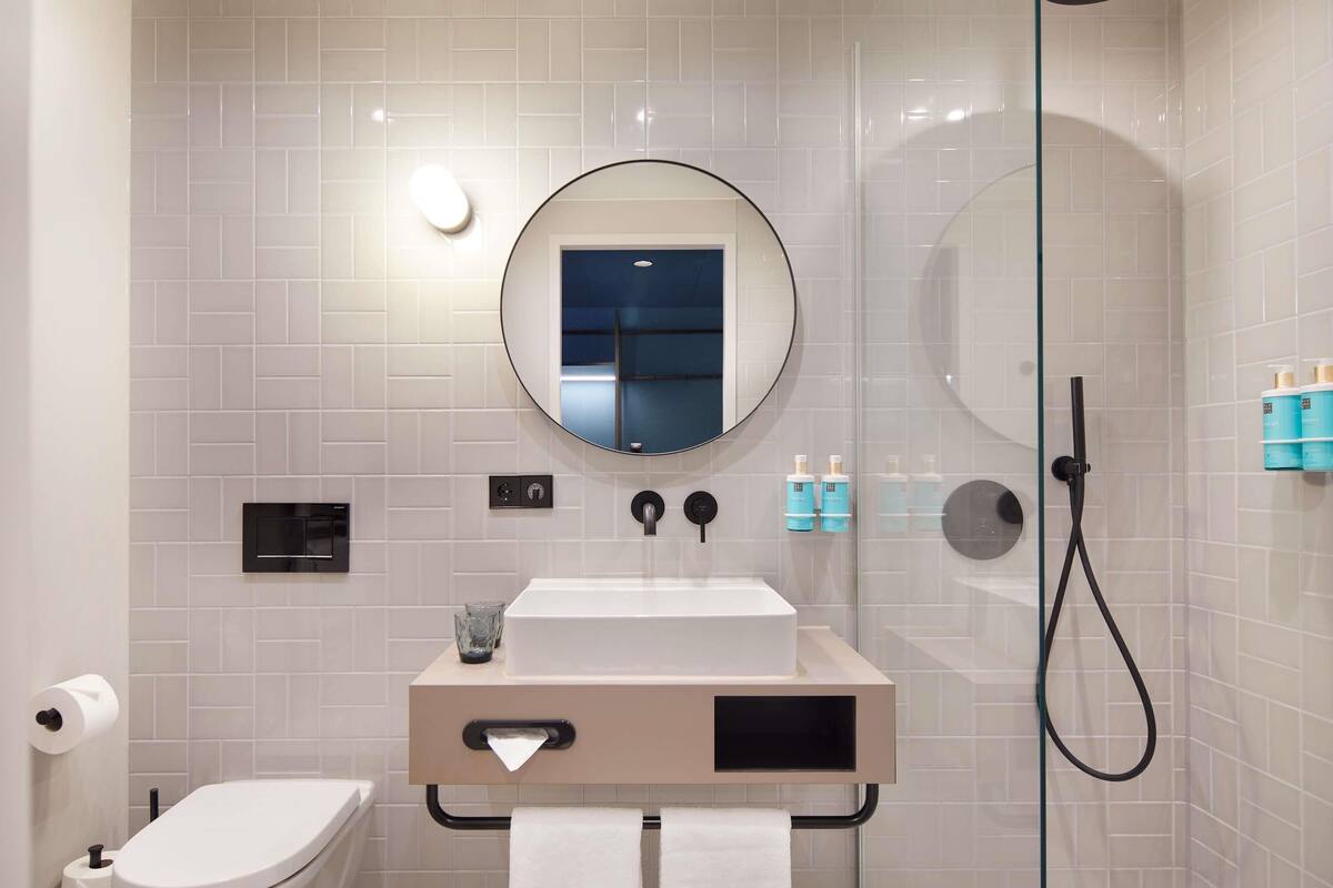 Une salle de bain moderne équipée de toilettes, d’un lavabo, d’un miroir et d’une douche à parois en verre.