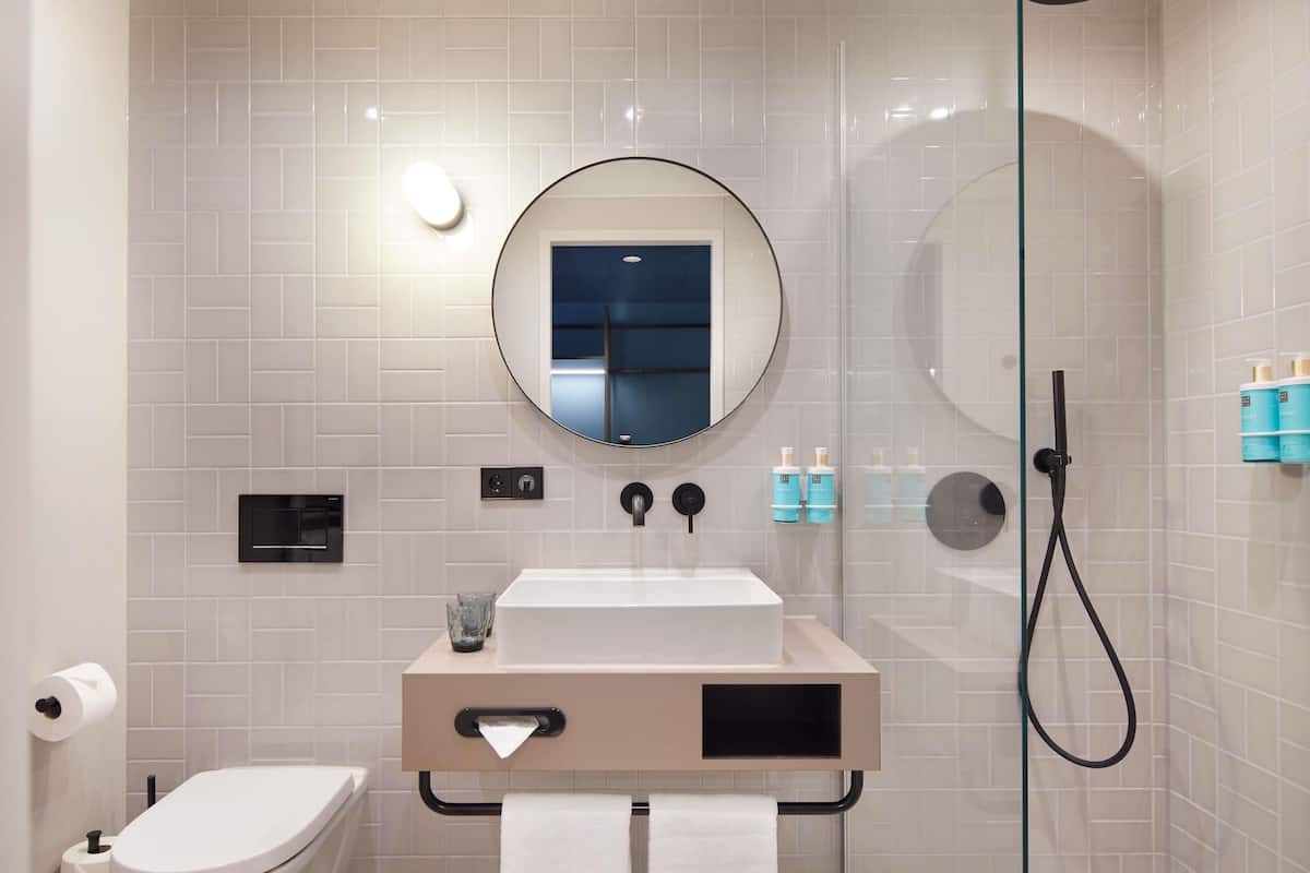 Une salle de bain moderne équipée de toilettes, d’un lavabo, d’un miroir et d’une douche à parois en verre.