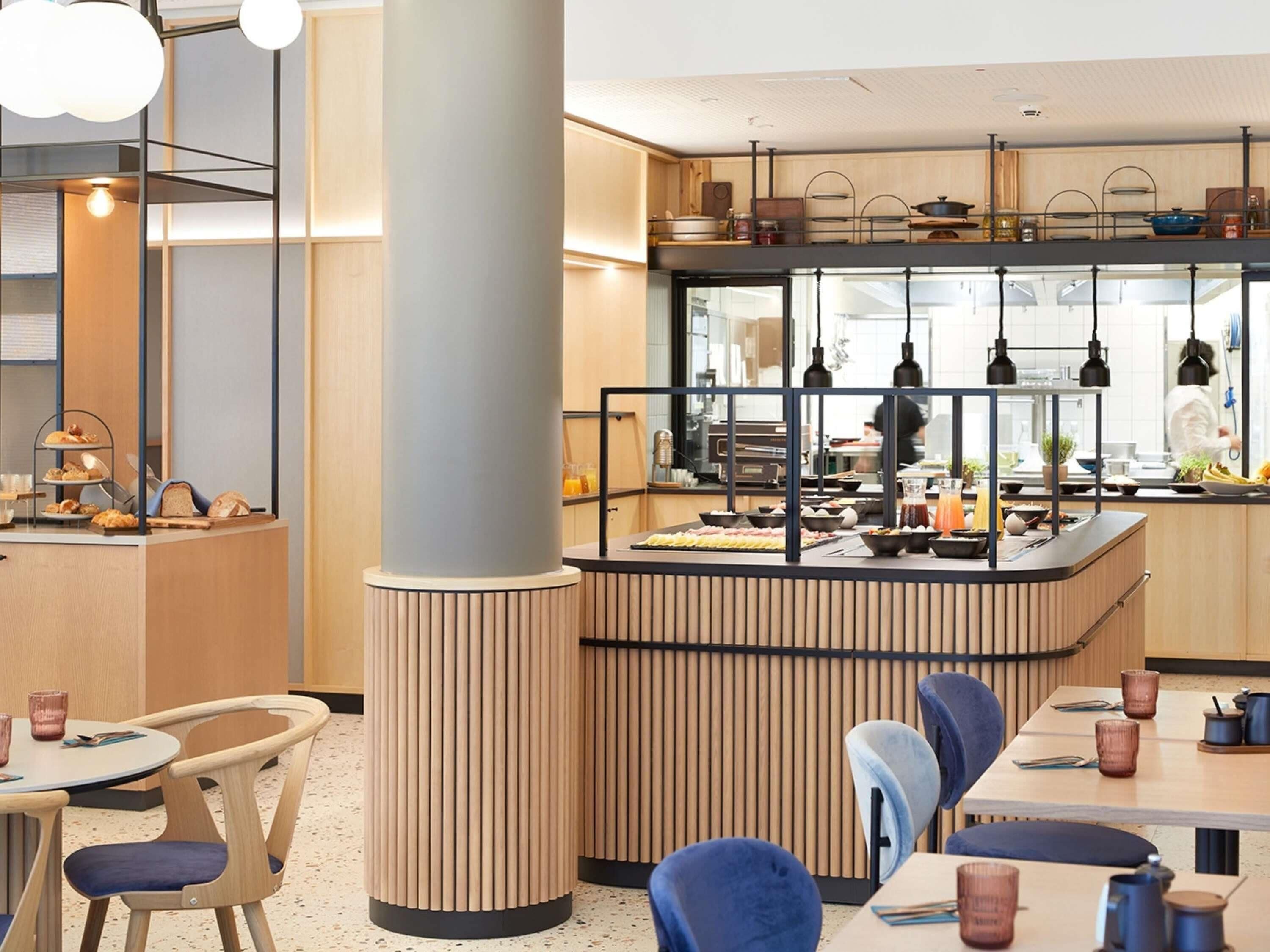 Ein modernes Restaurant mit einer zentralen Theke, Esstischen, Stühlen und Pendelleuchten.