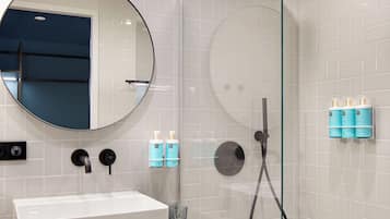 A modern bathroom with a glass-enclosed shower, a round mirror, a white sink, and two towels.