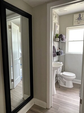 A bathroom with a white toilet, a pedestal sink, and a shelf with towels and toiletries.