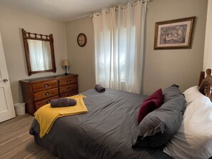 A bedroom with a bed, a dresser, a mirror, a clock, and a framed picture on the wall.