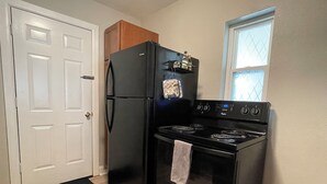 Una cocina con un refrigerador, estufa y horno negros. Se ve una puerta y una ventana con vistas.