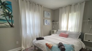 Un dormitorio con cama, mesita de noche, lámpara de pared, un cuadro y ventana con cortinas.