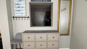 Una habitación con un aparador color beige, un espejo, un cartel que dice 'Coffee Bar' y una cortina con estampado de peces.