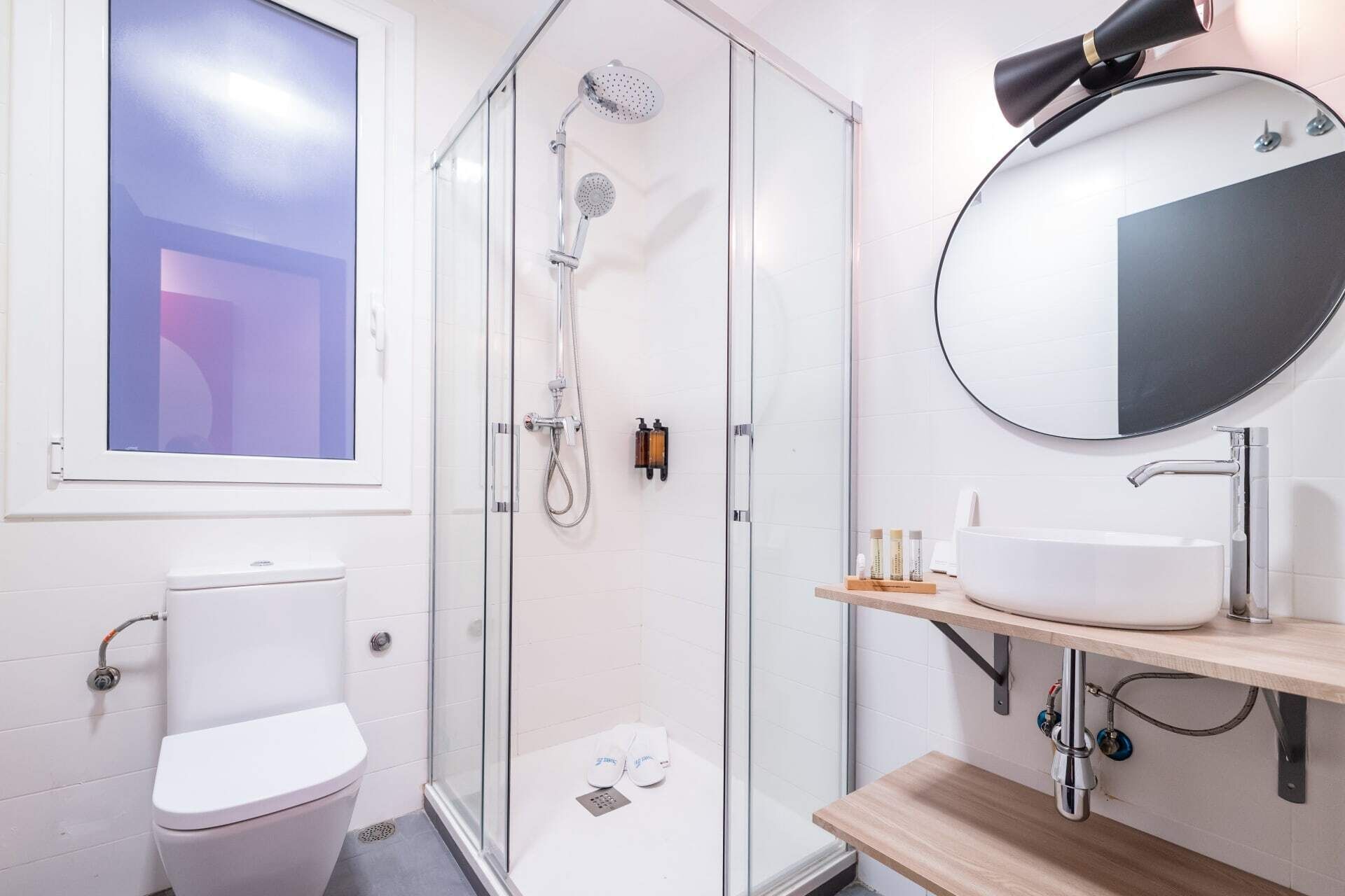 Ein modernes Badezimmer mit einer Duschkabine, einer Toilette, einem Waschbecken mit Spiegel und einem Fenster.