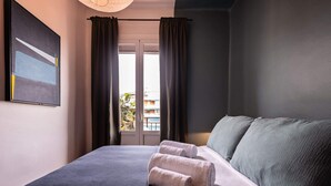 A neatly made bed with two rolled towels, a dark-colored headboard, and a window with curtains.