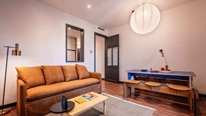 A modern living room with a sofa, a small table, a desk with chairs, a hanging light fixture, and a door. - Sweett | Aragon Park Miro 204 (Barcelona)