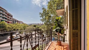 Un balcon donnant sur une rue de la ville, une plante en pot et un immeuble avec des volets.