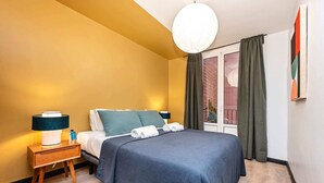 A hotel room with a bed, bedside tables, a lamp, and a view of the outside through a window with curtains.