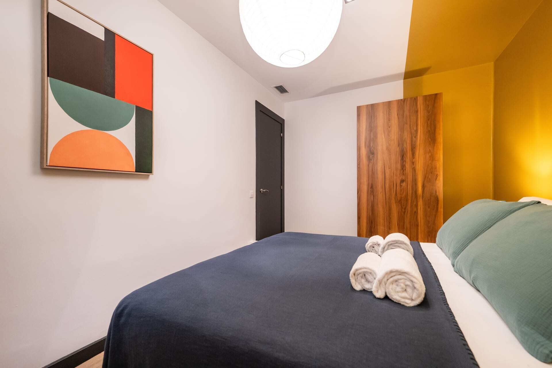 A hotel room with a bed, a wall art piece, a wooden panel, and a door.