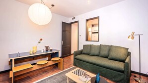 Una sala de estar moderna con un sofá verde, una mesa de centro de madera con un tablero de ajedrez, un escritorio con una lámpara y una lámpara colgante grande.