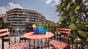 A round table with a blue box and a yellow object on it, surrounded by red chairs, with a view of a multi-story building in the background.