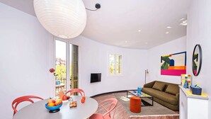 A modern living room with a round table, red chairs, a sofa, and a colorful abstract painting on the wall.