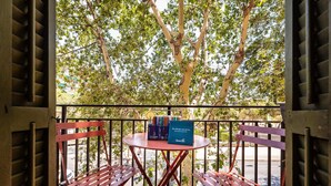 A balcony with a table and two red chairs, overlooking a tree-lined area. - Sweett | Aragon Park Miro Principal 4 (Barcelona)