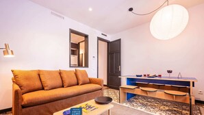 A modern living room with a sofa, a coffee table, a small desk, and a hanging light fixture. - Sweett | Aragon Park Miro Principal 4 (Barcelona)